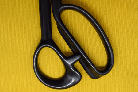 Black plastic scissors handle close-up. Scissors on a yellow background. Sewing equipment.