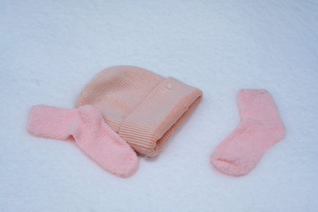 A pink woolen womans hat in the snow. Pink terry socks in the snow. Winter clothes in the snow.