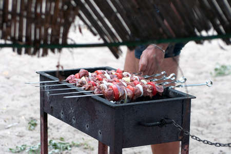 Barbecue outdoor on bright summer day. tasty juicy marinated pieces of meat, tomatoes, onions, peppers on skewers roasting on coal fire. Camping, holiday, delicious food, garden partyの写真素材