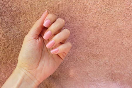 Female hand with pink nail polish on a pink background. Hand with folded fingers, manicure on a background of towels.の写真素材