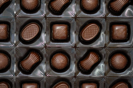 Assorted chocolates in a box top view. Sweets of different shapes made of black chocolate with...