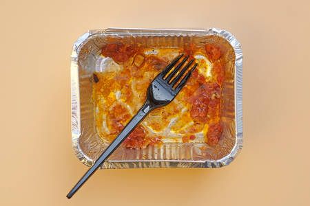 Food aluminum foil container with leftover food and black plastic fork. Disposable aluminum food container top view. Used dirty disposable tableware.の写真素材