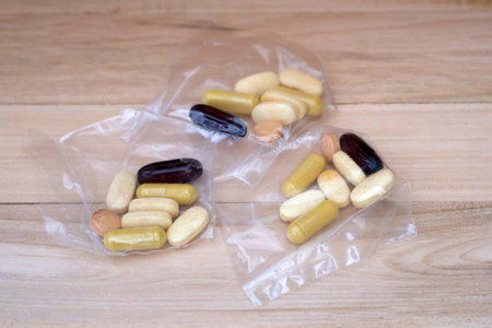 Pills in cellophane packs on a wooden background. Servings of tablets of different sizes and colors...