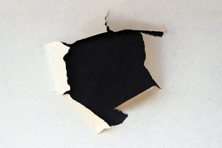 hole in white paper with black paper backing. Curled Tear on a black pasteboard paper. Concept, copy space for textures. Breakthrough paper holeの写真素材