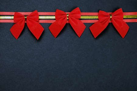 Christmas composition with a dark background. Red and gold ribbons with red Christmas bows.の写真素材