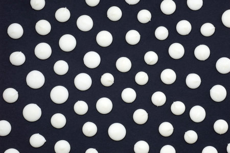Drops of white chocolate on a black background top view. Background from sweets. White chocolate for...