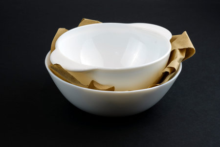Two deep white ceramic plates stacked one on top of the other. Tureens new with wrapping paper on a black background. White crockery made of impact-resistant material.の写真素材