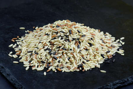 A mixture of brown, black, red and white rice. Dry long grain rice on a black background.の写真素材