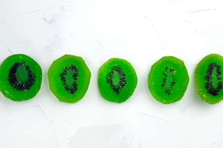 Candied kiwi fruits are laid out in a row on a white background top view. Dried kiwi slices in sugar syrup.の写真素材