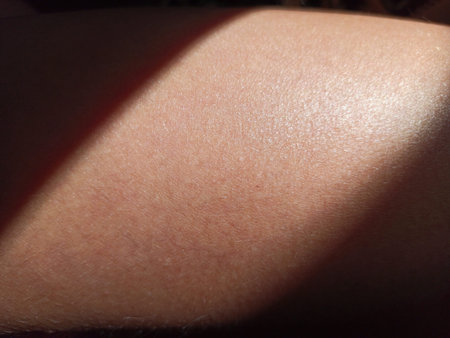 Thigh of a girl with a ray of sun. Close-up tanned skin in the shade.