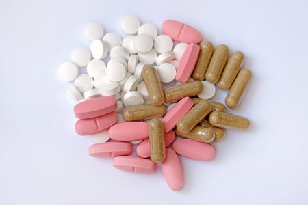 White round tablets, pink oval tablets and capsules on a white background. Food supplements in the...