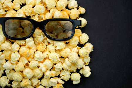 Popcorn and glasses for watching movies in 3d format on a black background. Cinema theme, background with place for text. Face with glasses made of popcorn top view.の写真素材