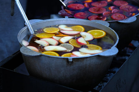 Large cauldron with mulled wine and fruit. Apples, spices and citrus fruits in a pan with mulled wine. Oranges and apples in wine close-up. Street food and drinks during the fair.の写真素材
