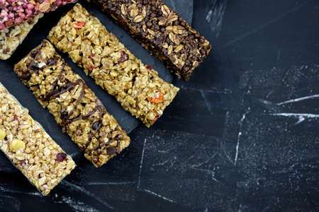 Oatmeal bars with berries and cornflakes. Healthy nutritious snacks. fitness bars on black background top view with place for text. Delicious and healthy food. Granola bars assortmentの写真素材