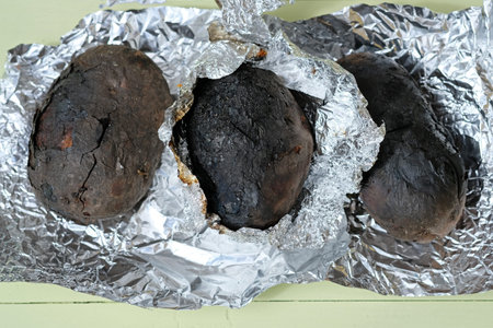 Baked potatoes in a peel on charcoal. Three potatoes in foil baked over a fire. Baked potatoes with...
