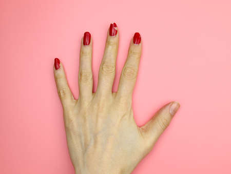 Peeling nail polish. Girl's hand with red nail polish without manicure top view. Not well-groomed hands on a pink background.の写真素材