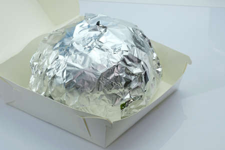Hamburger in foil and cardboard box on a white background. The burger is wrapped in foil to keep it warm. fast food delivery.の写真素材