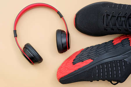 Headphones red and black sneakers on a beige background top view. Sports activities with music. Stylish wireless headphones with sports shoes.の写真素材