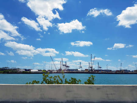Seaport in Miami through the fence on the highway in the US in the summer. Port cargo cranes in Florida view from the road across the seaのeditorial素材