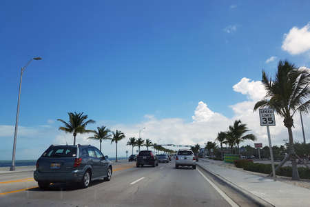 Traffic in the USA with palm trees along the road on a clear day from a traveler car window. Road to Miami in hot weather with clouds and blue skyのeditorial素材