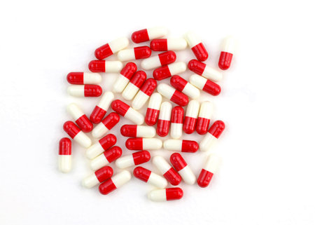White and red pill capsules on white background. Herbal supplement in capsules. Vitamins in gelatin...