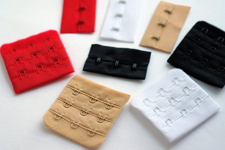 colored hooks on a fabric basis. Colored bra clasps on a white background top view. Accessories for...