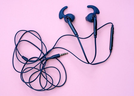 Wired blue earphones on a pink background. Headphones with silicone pads. Ear pads for earphones. Headphone cord with microphone.の写真素材