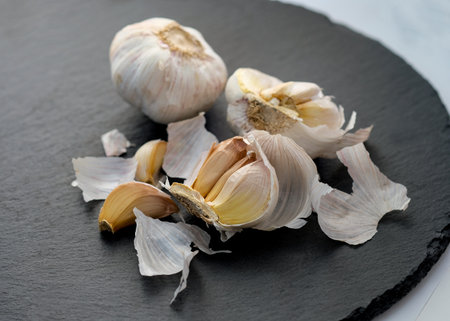 Garlic on a black background top view. Two heads of garlic, one whole, the other divided in half. Dry garlic with yellow edges.の写真素材