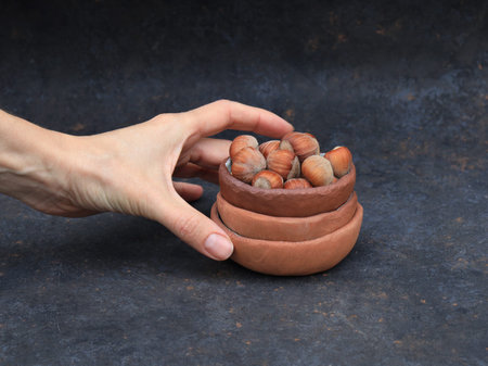 Small red clay bowls, handmade in a rustic wabi-sabi style. The top bowl is filled with hazelnuts,...