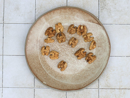 Top view of a handmade rustic stoneware plate with natural speckles. Scattered whole walnuts...