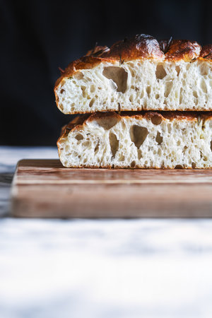 Two slices of focaccia bread stacked on a wooden board, showing the light and airy texture of the bread with a dark background for contrast.の写真素材