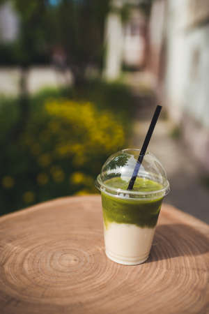 A glass stands on a wooden table against a background of green grass and yellow dandelionsの写真素材