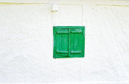 Closed green wooden window shutters on an old whitewashed wall.