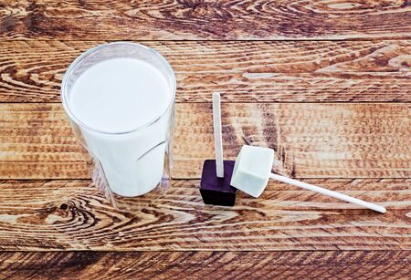 Dark and white chocolate stirrers near a glass of milk on a wooden table.の写真素材