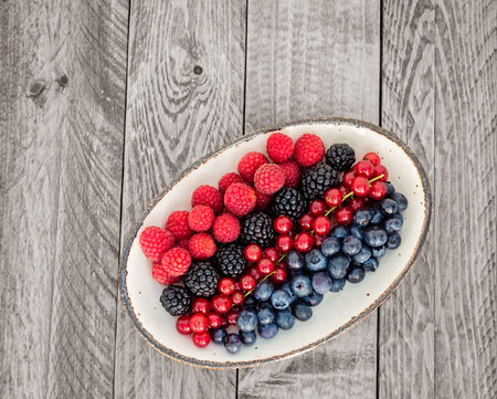 Blueberries,raspberries,redcurrant and blackberries on an oval plate on a wooden table.