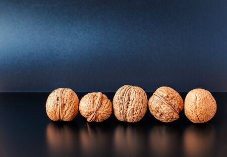 Five walnuts in a row on a dark table against a dark blue background.の写真素材