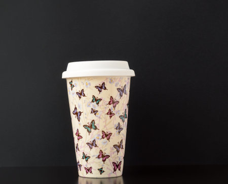 Lid on ceramic insulated cup with colorful butterfly pattern on dark gray background.の写真素材