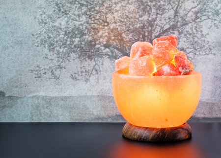 Turned on Himalayan pink salt lamp carved as a bowl on a black table.の写真素材