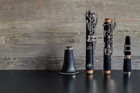 Black clarinet dismantled in four parts on a black table with a gray weathered wooden backgroundの写真素材