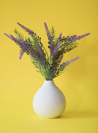 A bouquet of lavender flowers in a white vase. Yellow backgroundの写真素材