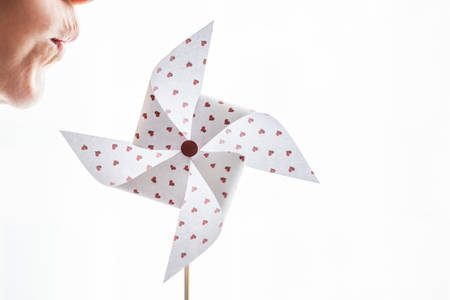 Woman blowing a hearts paper pinwheel isolated on white backgroundの写真素材