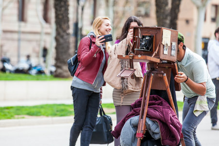 Young male photographer taking pictures using a vintage wooden camera at the Triumphal Arch in Barcelonaのeditorial素材