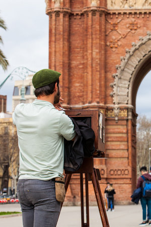 Young male photographer taking pictures using a vintage wooden camera at the Triumphal Arch in Barcelonaのeditorial素材