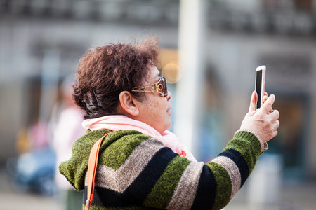 Asian tourists using their cellphones to take pictures at Dam Square in Amsterdamのeditorial素材