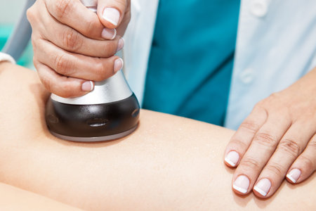 Doctor performing an  ultracavitation treatment on a young female patient leg