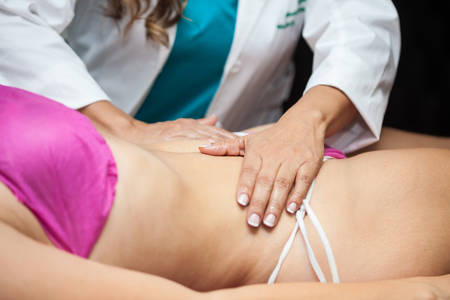 Doctor performing an abdominal massage on a young female patientの写真素材