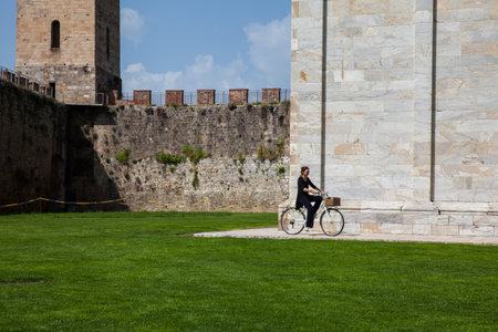 Woman biking next to the ancient walls of Pisa and Monumental Cemetery at the Square of Miracles in a beautiful early spring dayのeditorial素材