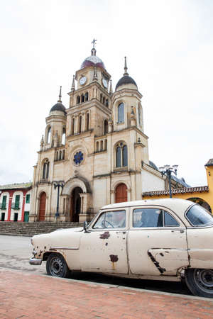 Antique rusty car parked next to the Parish Church of the small town of Ventaquemada in Colombiaの写真素材