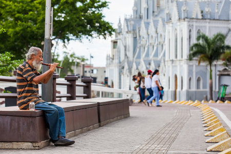 CALI, COLOMBIA - OCTOBER, 2019: Old man playing his flute to get money at the River Boulevard in Caliのeditorial素材