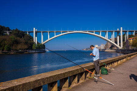 PORTO, PORTUGAL - MAY, 2018: Man fishing close to the Douro River mouth and the Arrabida Bridge in a beautiful early spring day at Porto City in Portugalのeditorial素材